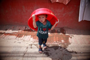 A little boy plays with a plastic wash basin on a hot Friday afternoon in Patan.