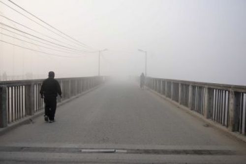 A man walks past the Teku-Sanepa bridge in a misty morning
