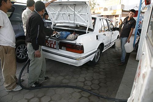 Back door entry: A car owner fills petrol in extra jars at a petrol pump in Basbari on Tuesday.