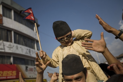 A child waves a Nepal state flag as a crowd hoist him up. The crowds have gathered outside the royal palace to demand that the King evacuate immediately.