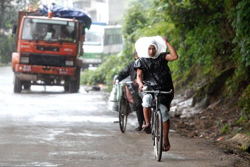 RAINDROPS ON MY HEAD: A cyclist rushes home with a make-shift raincoat as the monsoon broke through on Wednesday evening in Balaju, Kathmandu.