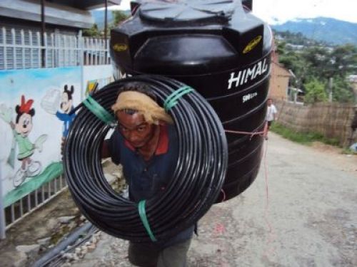 HEAVY WEIGHT: A labourer transports water pipes and tank from a hardware store to the customer's house on Monday in Dhankuta. PIC