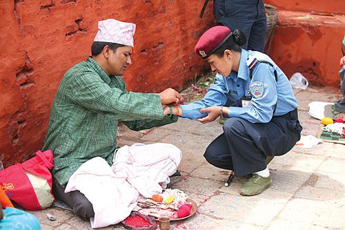 KNOTTY COP:A police woman takes a break from work to have a ritual thread tied around her wrist during Janai Purnima on Wednesday in Kumbeshwor Temple.