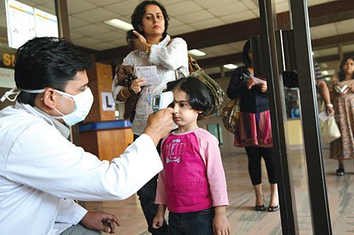 STICK 'EM UP: A health worker at Kathmandu airport testing a young passenger for signs of swine flu on Monday. The manual testing and filling of health forms results in huge queues at immigration.