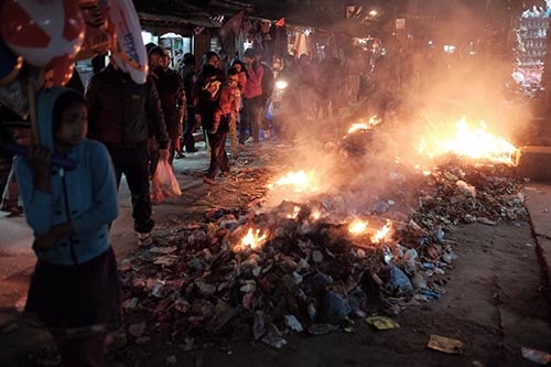 People walk past a burning pile of garbage at Mangal Bazar on Tuesday. Garbage in the area has not been collected for the past six days.