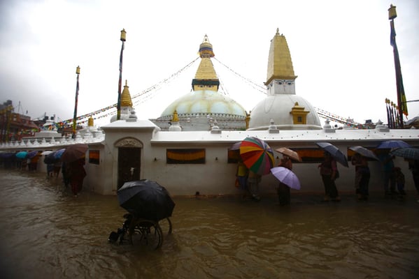 Pedestrians have a difficult time getting across a flooded street during a downpour in Boudha, Kathmandu on Sunday.
