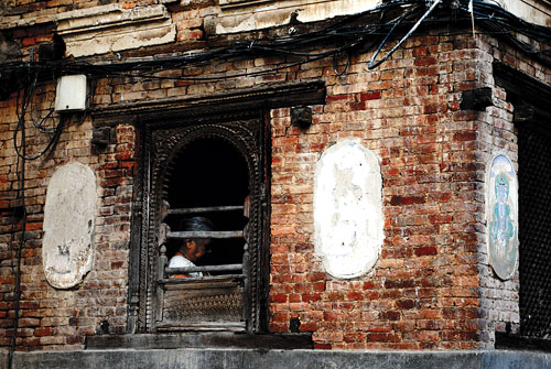 SNEAK PEEK: A woman sits behind a traditional Newari balcony in Patan Durbar square.