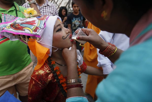 A woman offers milk to a boy dressed as a 'cow' on the occasion of Gai Jatra festival in Kathmandu on Tuesday. On this day, people dress up as cows and ascetics to commemorate family members who have died in the past year.