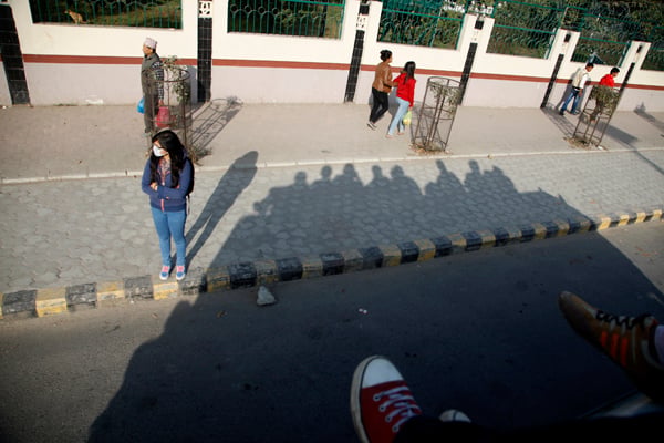 A girl waits for the bus in New Baneswor, Kathmandu on Tuesday as an over-crowded bus passes by her. As fuel crisis caused by India's blockade of Nepal persists, commuters in Kathmandu Valley are forced to travel sitting on the roofs of the jam-packed buses.