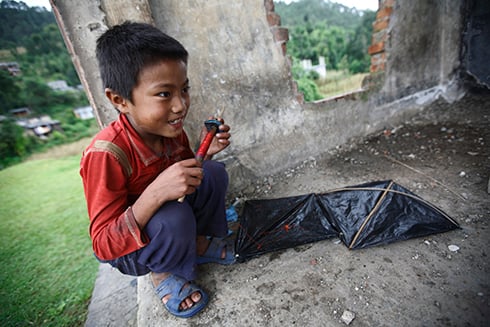 FLIGHT OF FANCY: A boy plays mends a kite in Sindhupalchok. The building was a training centre for Nepal Police before being bombarded during the insurgency.