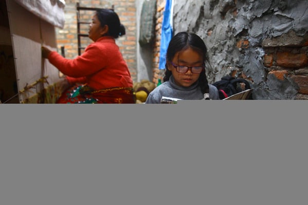 Seven-year-old Sumita Yonjan reads a book as her mother Fulmaya Tamang weaves a carpet in a carpet factory at Banglamukhi, Lalitpur on Sunday.