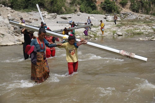 Earthquake survivors crossing Rosi Khola in Timal village of Kavre district, carrying tin sheets to rebuild their houses.