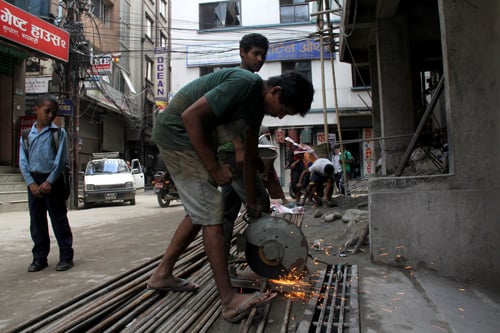 A child looks at a worker cutting iron in a construction site at Sundhara on Friday.