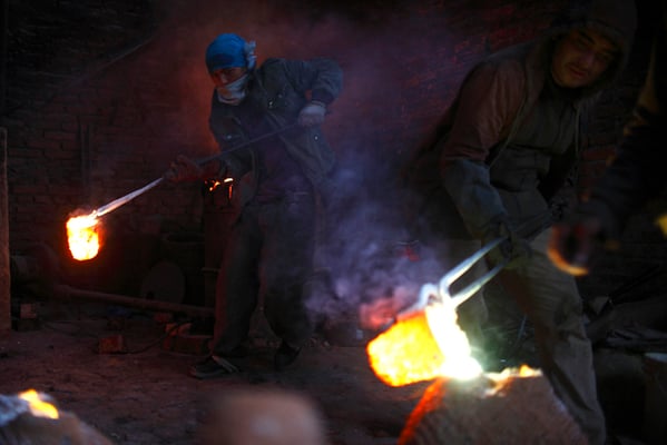 Twenty-five-year-old Radheshyam Khadka and twenty-three-year-old Dev Kumar Sanjel pour molten copper into a clay mould at a workshop in Lalitpur on Wednesday.