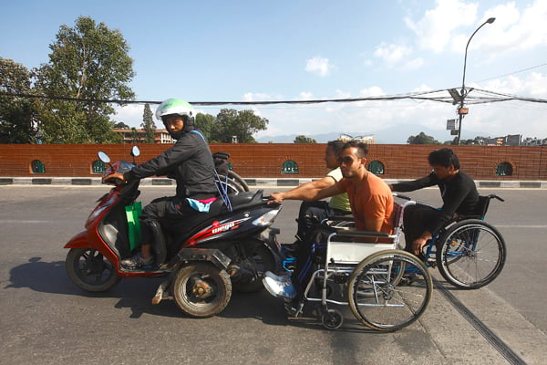 A person riding a disabled-friendly scooter pulls wheel-chairs of his physically-disabled friends in Kathmandu. Import of petroleum products has been eased this week but refueling centres are still not distributing fuel for private vehicles in Kathmandu.