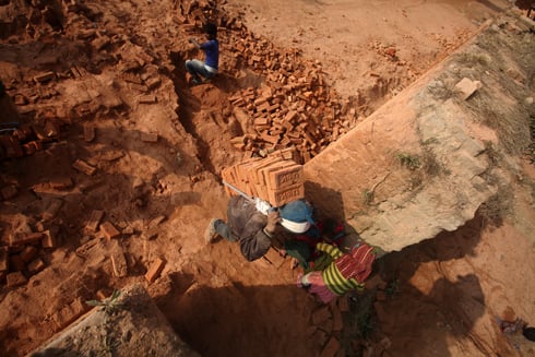 BUILDING BLOCKS: A worker carries baked bricks away from the chimney at a brick kiln in Bungmati on Monday.