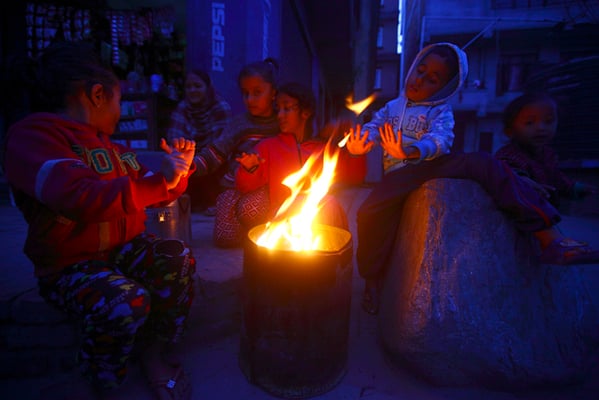 Children huddle beside a fire to keep themselves warm at Lalitpur on Sunday.