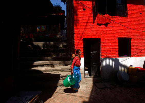 A woman carries her baby on her back as she goes to fetch water at a nearby tap in Bhaktapur on Monday.