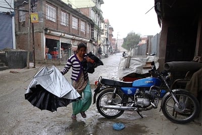 BLAME IT ON THE RAIN: A woman takes shelter after her umbrella turns inside out due to strong winds and showers in Nakhu on Thursday.