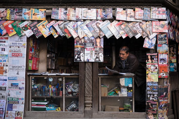 A man reads a newspaper at his store in the morning in Patan on Monday.