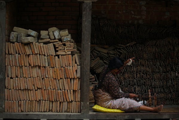 An elderly woman makes cotton wicks by a pile of roof tiles of a temple destroyed in last year's earthquake in Lalitpur on Thursday.