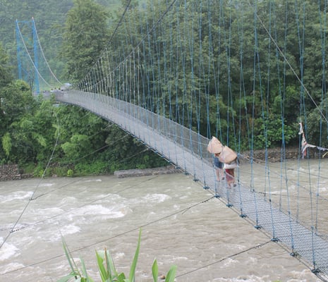 A couple cover themselves from rain using 'shyakhu', a traditional raincoat made of bamboo, as they cross the Mardi river in Pokhara on Friday.